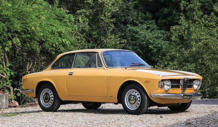 Alfa Romeo Giulia GT Junior 1600 Jaune sur des gravier devant des buissons