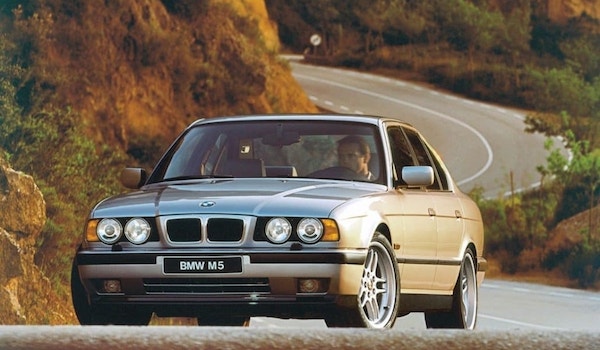 BMW M5 E34 gris clair sur une route sinueuse