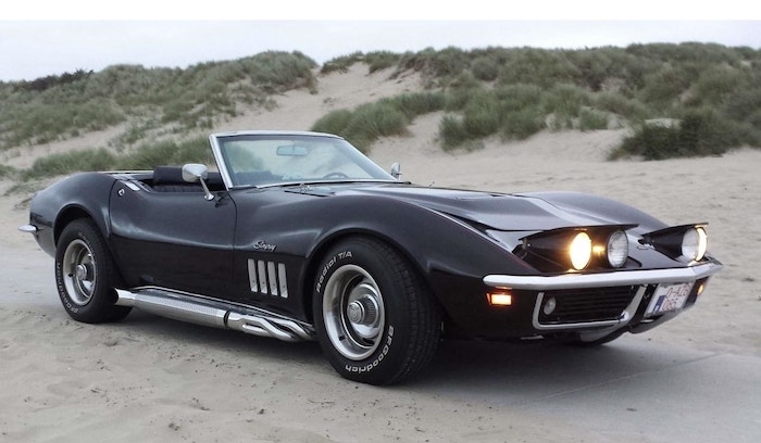 Corvette C3 cabriolet noire de 3/4 face sur une plage au crépuscule