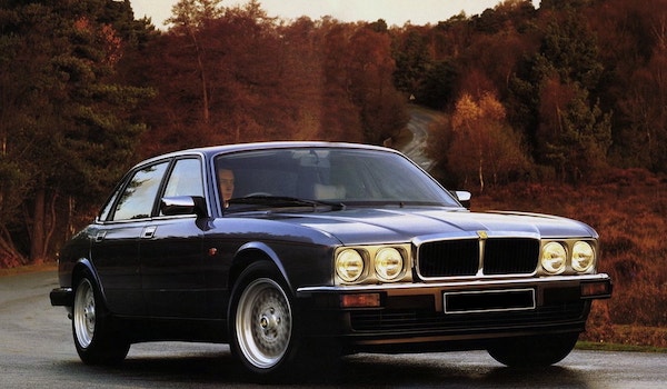 Jaguar XJ40 gris foncé sur une route boisée en automne