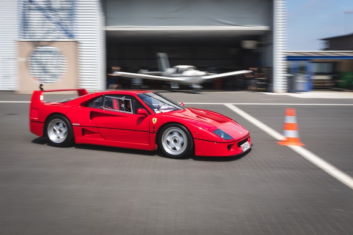 Ferrari F40 rouge en mouvement devant un hangar d'aviation