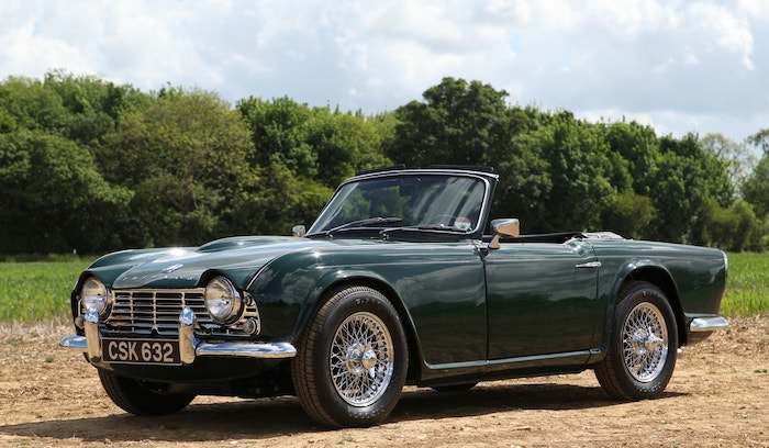 Triumph TR4 vert anglais décapotée devant un champ