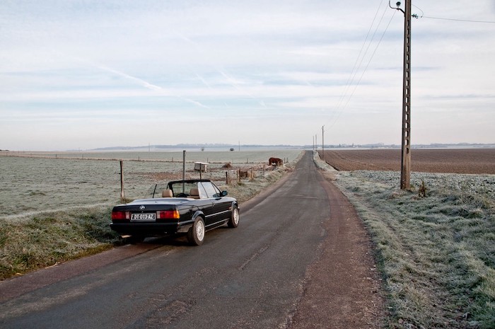 BMW E30 cabriolet sur une route de campagne de 3/4 arrière