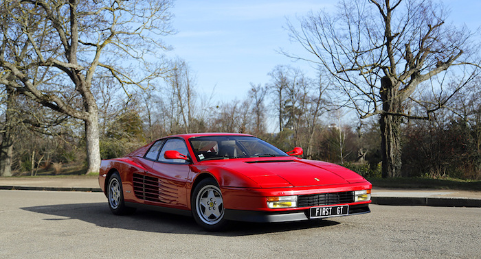 Ferrari Testarossa rouge de 3/4 face devant une zone boisée