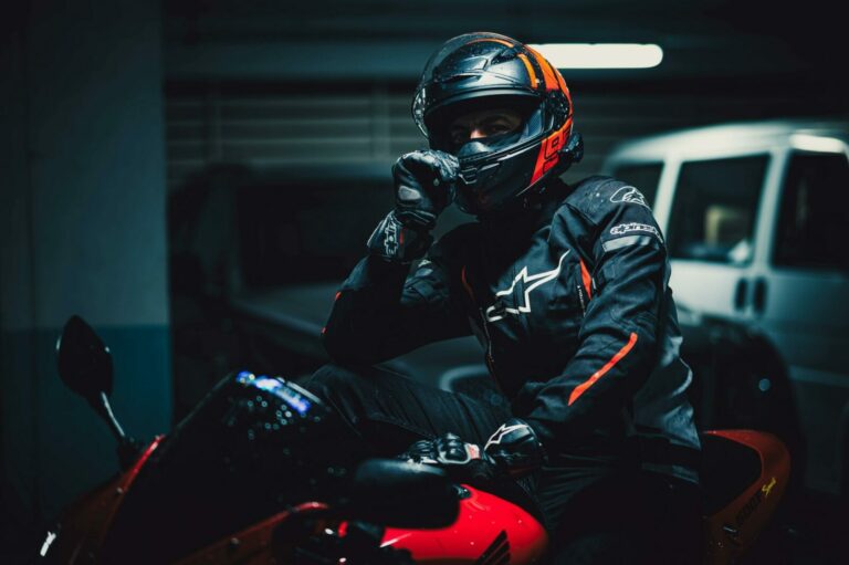 Motorcyclist in protective gear poses on red bike in dimly lit urban garage.