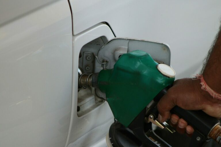 Close-up of a hand refilling a car's gas tank at a station with a green fuel nozzle.